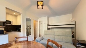 Ein kompakter Wohnraum mit Küchenzeile, Esstisch, einer Couch und einem Etagenbett.