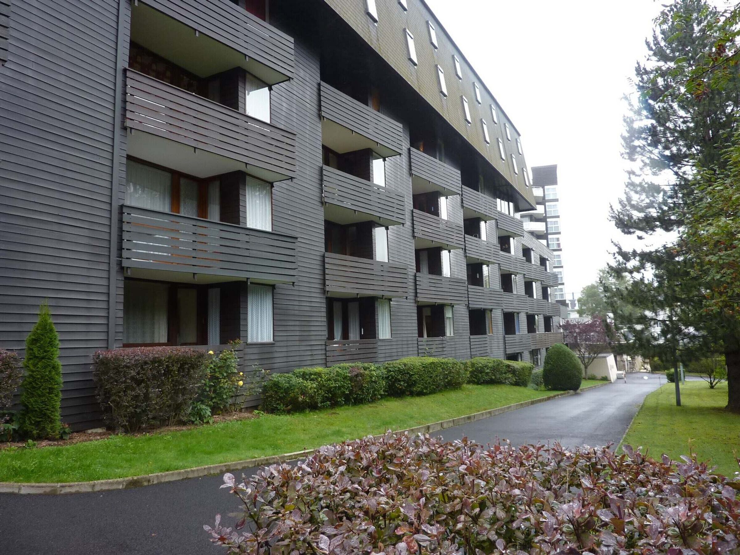 En flere etagers boligbygning med altaner og en belagt indkørsel.
