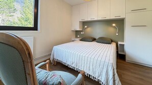 Ein Schlafzimmer mit Bett, Stuhl, Fenster und einer Pendelleuchte.