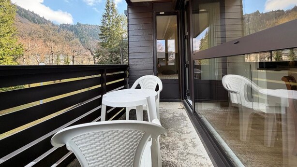 Ein Balkon mit zwei weißen Plastikstühlen und einem Tisch, der auf eine gebirgige Landschaft blickt.