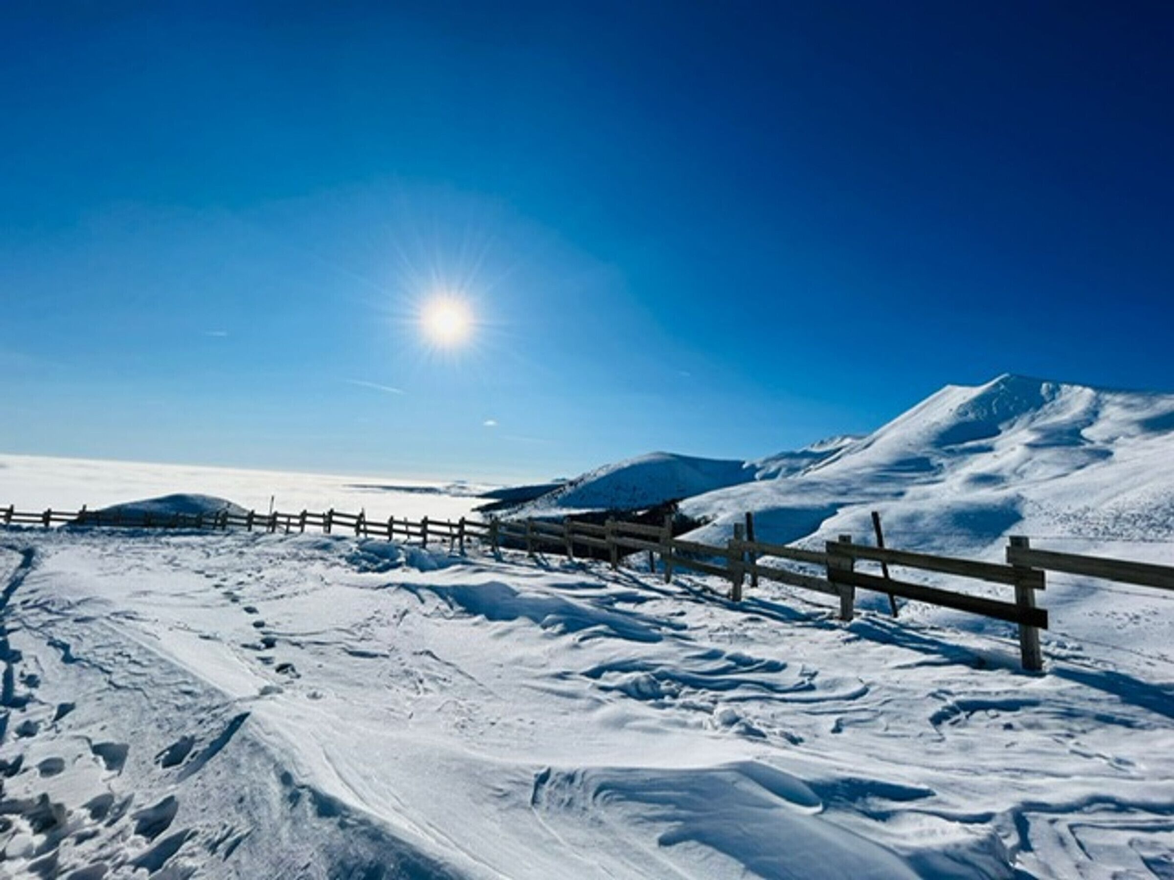 Paisaje nevado con cerca de madera y cielo azul despejado.