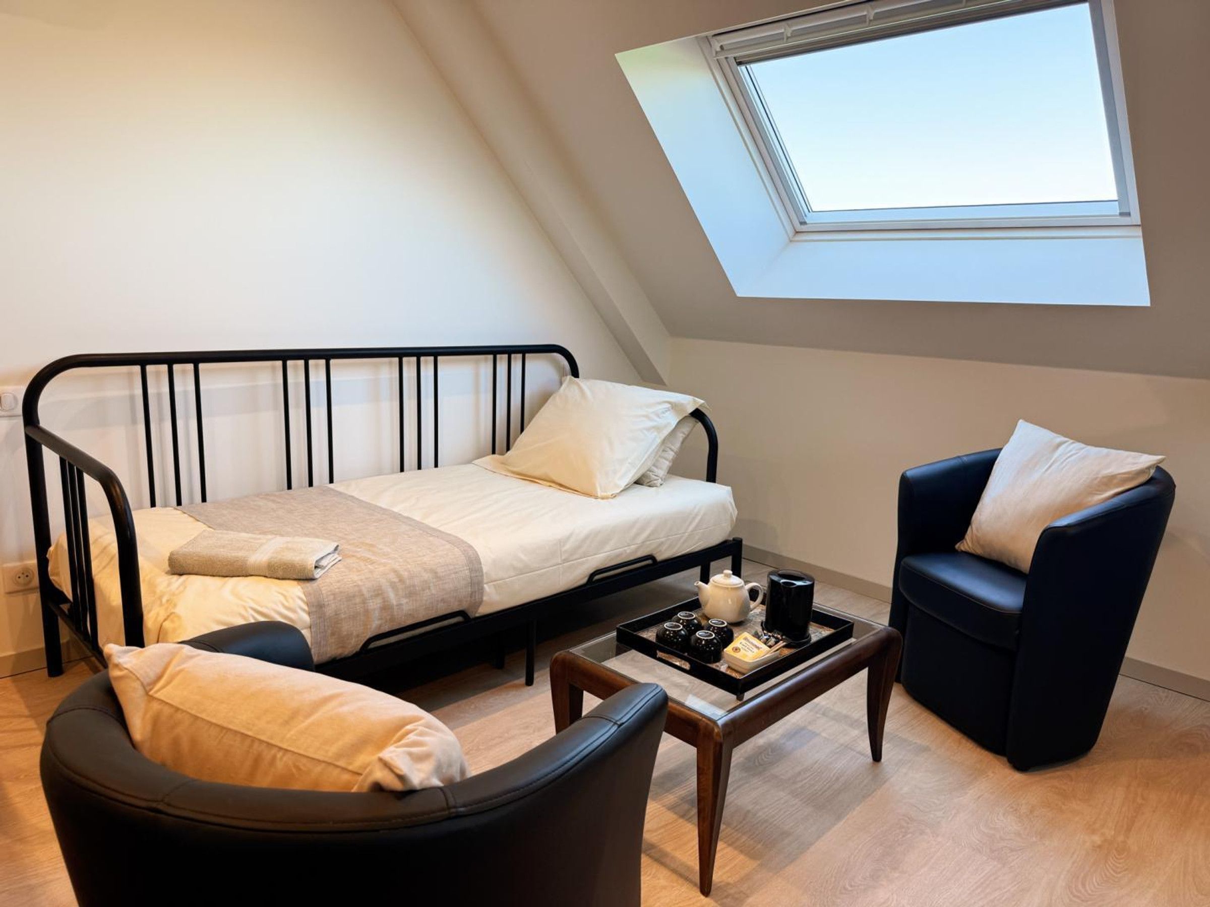 Une petite pièce agréable et chaleureuse, avec un lit, une chaise, une table basse et une lucarne.