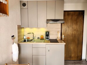 A compact kitchen with a sink, a coffee maker, and a wooden door. - Studio with balcony, pets welcome - 4 guests (Samoëns)