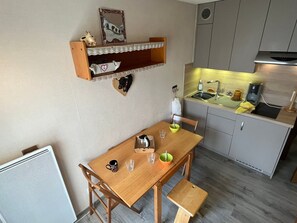 A compact kitchen with a wooden table, chairs, a small shelf with decorative items, a sink, and a coffee maker. - Studio with balcony, pets welcome - 4 guests (Samoëns)