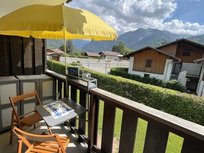 A balcony with a table and chairs, a yellow umbrella, and a view of houses and mountains. - Studio with balcony, pets welcome - 4 guests (Samoëns)
