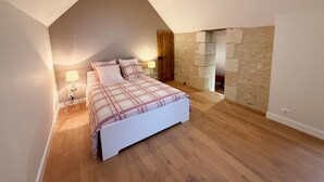 Une chambre avec un plafond en pente, un lit recouvert d’une couverture à carreaux, deux lampes de chevet et un mur en pierre.