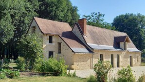 Une maison en pierre avec un toit en pente, de nombreuses fenêtres et un jardin à l’avant.