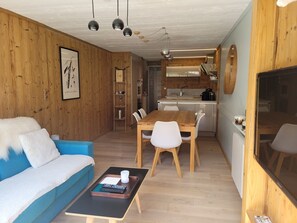 Ein kompakter Wohnraum mit Sofa, Esstisch, Stühlen, Küchenzeile und Fernseher.