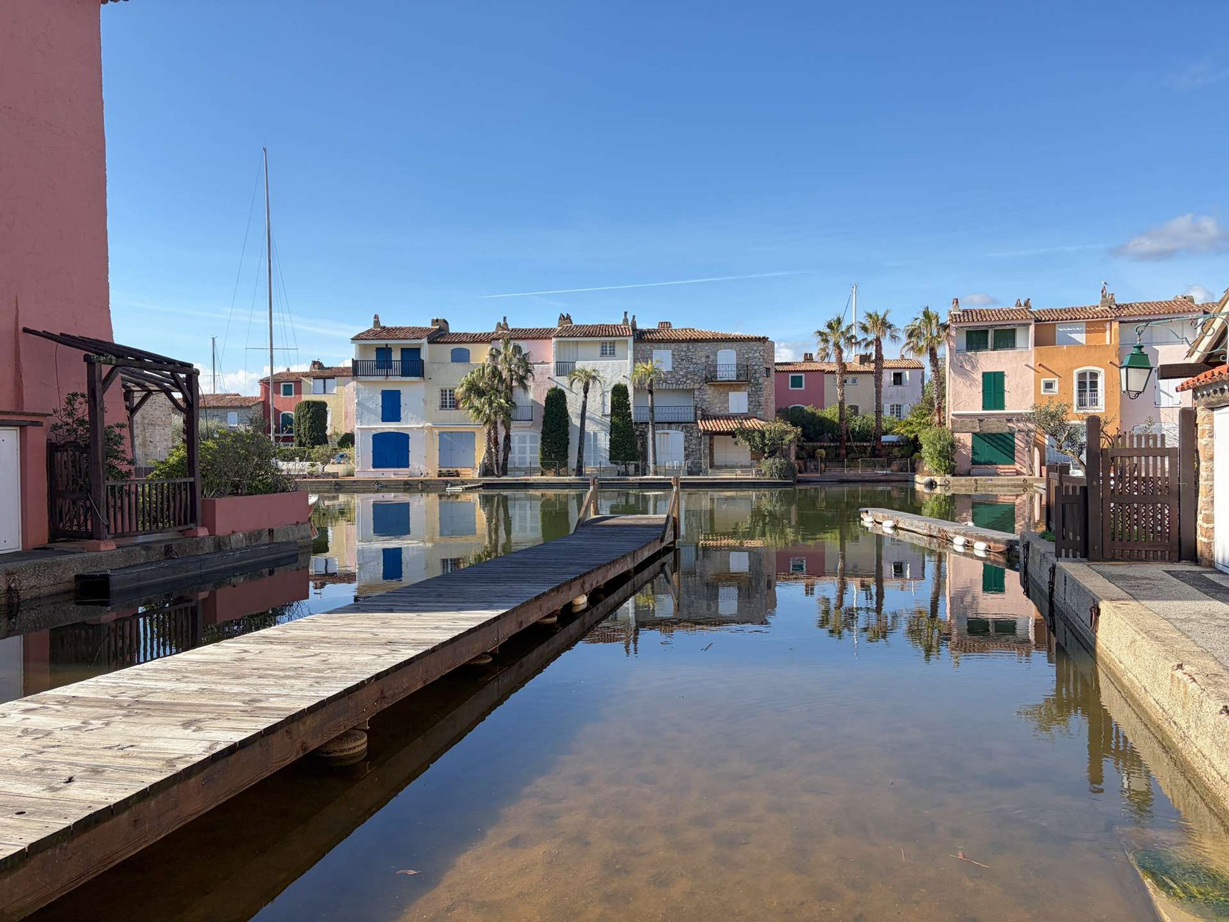 Un canal bordé de bâtiments des deux côtés, une jetée en bois et un ciel bleu azur.