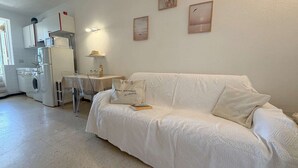 Sala de estar blanca con sofá, mesa y lavadora. Hay dos cuadros en la pared.