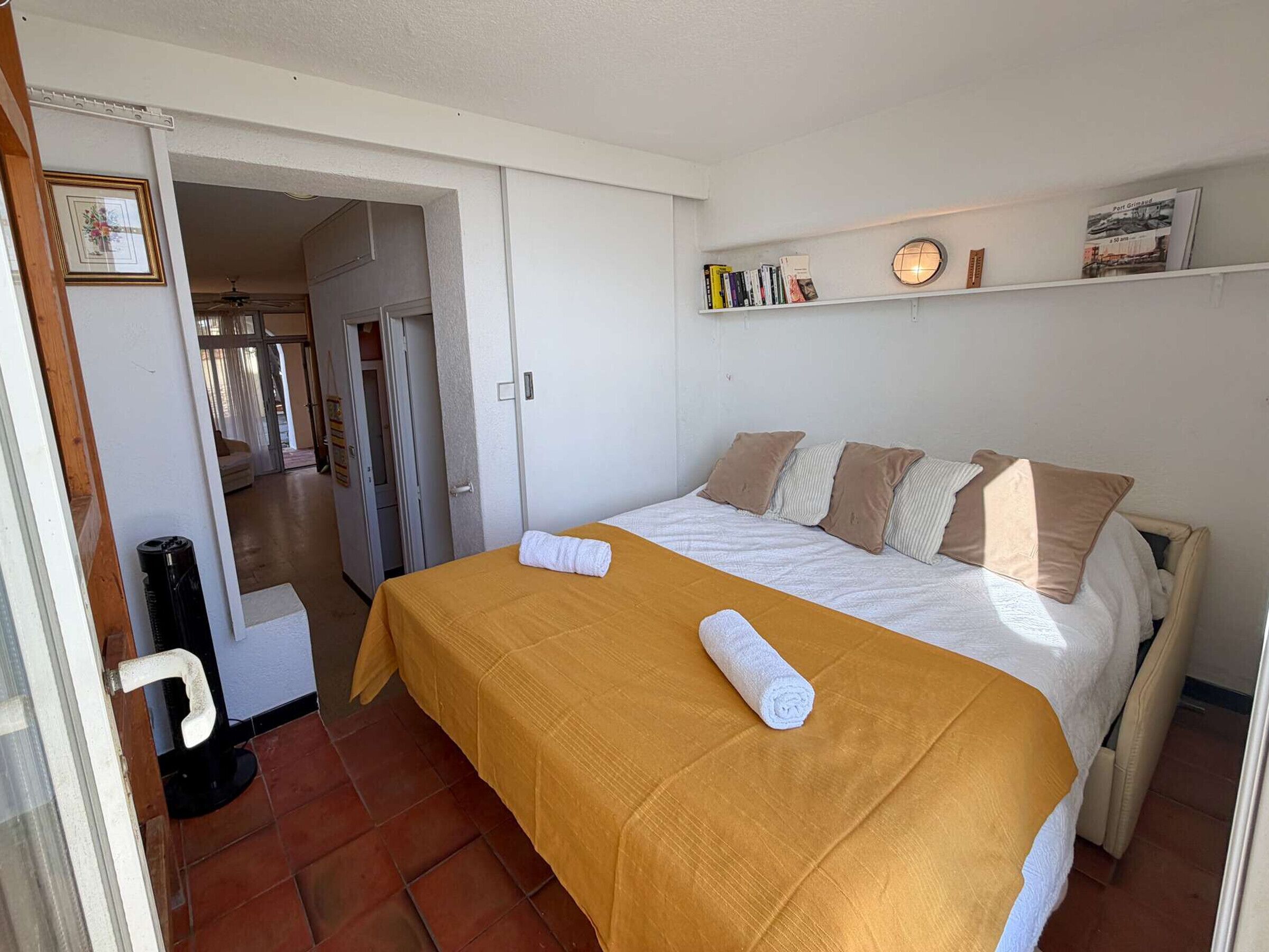 Ein Schlafzimmer mit einem Bett, einem Nachttisch, einem Regal mit Büchern und einer Tür zu einem anderen Raum.