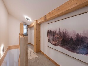 Ein Flur mit Holzbalken, einem gerahmten Kunstwerk mit einem Bären im Wald und einer Tür zu einem anderen Raum.