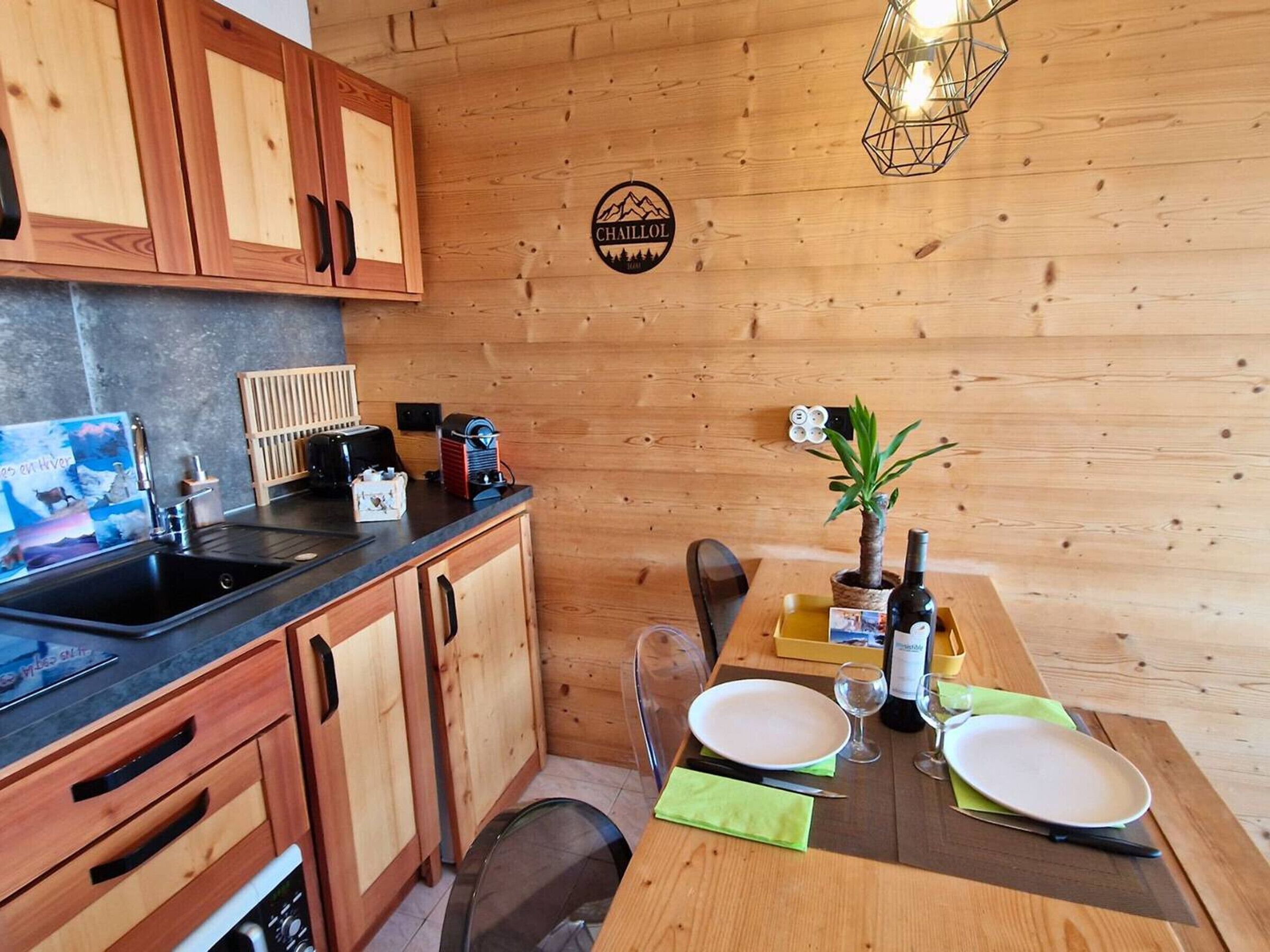 A wooden interior with a kitchen area, a dining table set for two, and a logo on the wall.