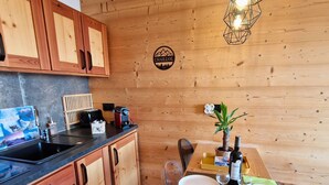 Un interior de madera con zona de cocina, una mesa de comedor para dos personas y un logotipo en la pared.