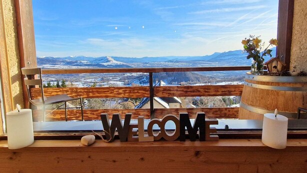 Un balcón de madera con un letrero que dice 'WELCOME', una vela y vistas a un paisaje nevado.