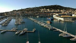 Una marina con numerosas embarcaciones amarradas, un puerto con edificios y una colina al fondo.