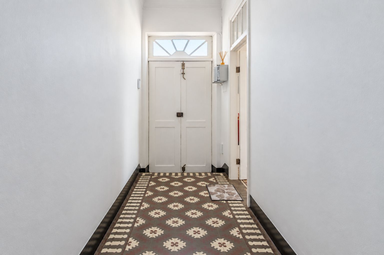 A hallway with a patterned carpet leading to a white door with a small window above it.