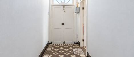A hallway with a patterned carpet leading to a white door with a small window above it.