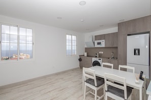 Cocina moderna con lavadora, microondas y refrigerador. Hay un comedor con mesa y sillas.