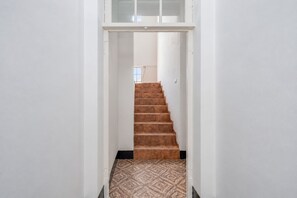 A narrow hallway with a staircase leading to a room with a window.