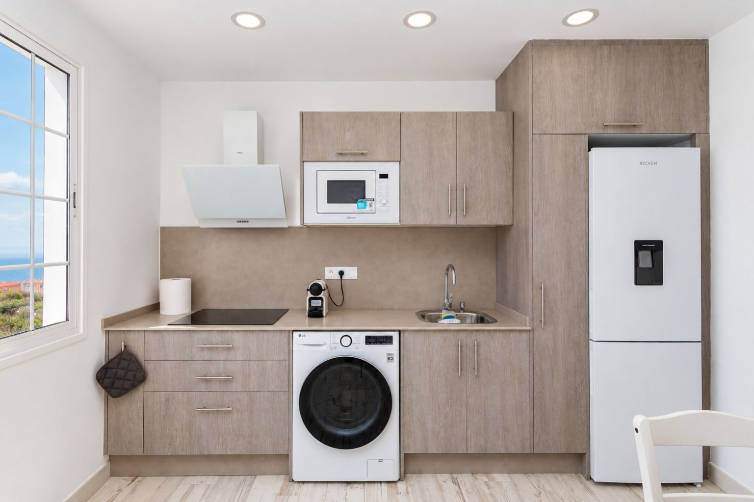 A modern kitchen with a washing machine, a microwave, a sink, and a refrigerator.