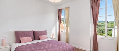 A bedroom with a bed, nightstand, lamp, and curtains.