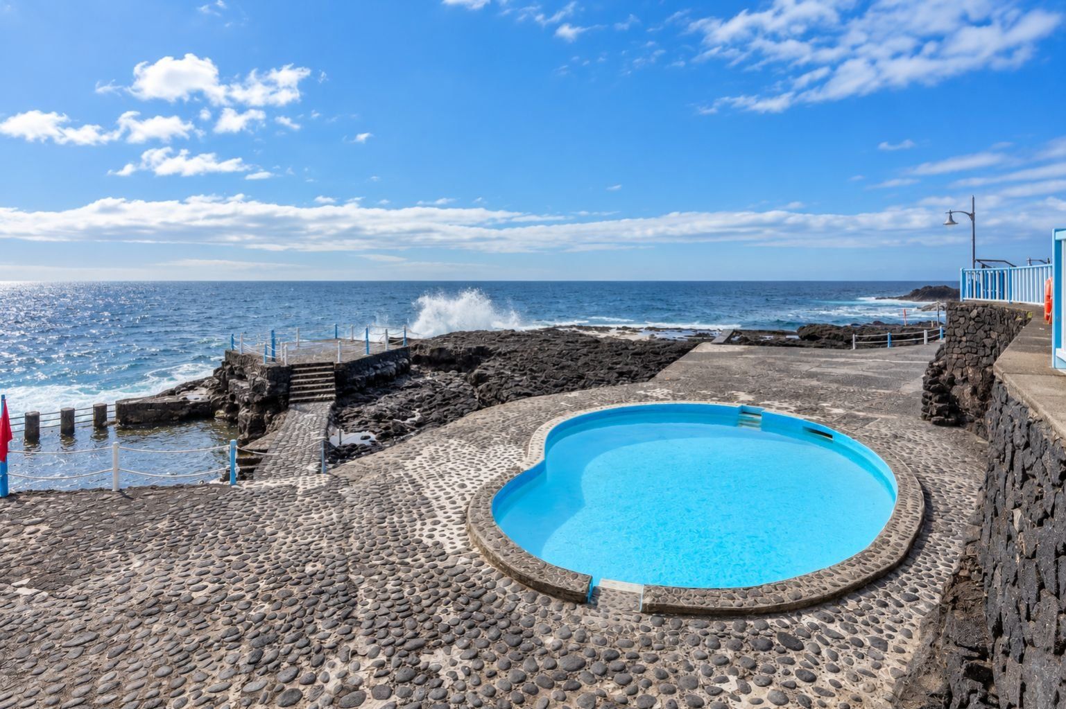 A pool with a stone pathway leading to the sea, a stone wall, and a clear view of the ocean.