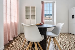 Un comedor con una mesa redonda, dos sillas, un aparador con puertas de cristal y una ventana con cortinas.
