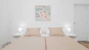 Une pièce minimaliste comprenant un lit, deux tables de chevet, un tableau accroché au mur et une porte.