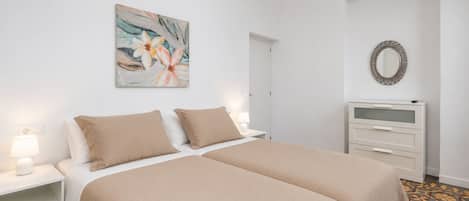 Un dormitorio con cama doble, mesitas de noche con lámparas, cómoda, espejo y un cuadro con motivos florales en la pared.