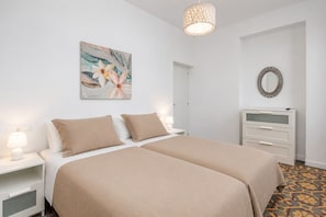 Un dormitorio con cama doble, mesitas de noche con lámparas, cómoda, espejo y un cuadro con motivos florales en la pared.