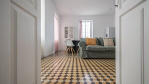 Une pièce avec un sol à motifs géométriques, un canapé avec des coussins, une table à manger avec des chaises et une fenêtre avec des rideaux.