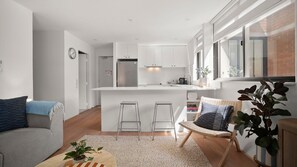 Una cocina moderna con armarios blancos, una isla central y una zona de comedor con taburetes de bar.