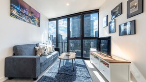 A modern living room with a sofa, coffee table, and TV, large windows with a city view, and framed pictures on the wall. - The Viewpoint Suite Southbank (Southbank)