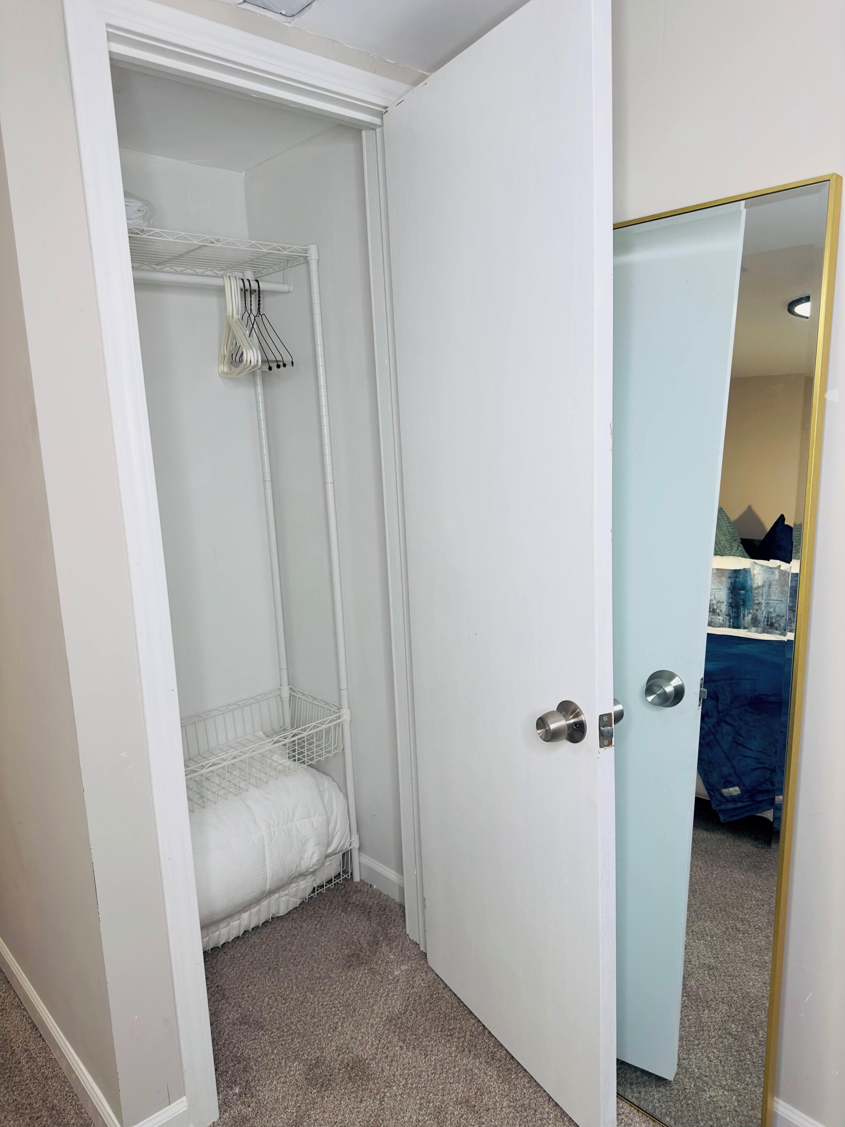 A room with a white door, a closet with a hanging rack, and a blue door leading to another room.