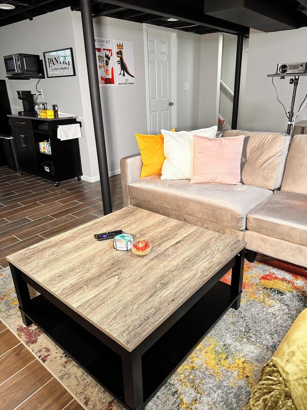 A living room with a wooden coffee table, a sofa with colorful cushions, a black TV stand, and a poster on the wall. - Quiet Bay View Getaway (Milwaukee)