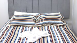 Una cama con ropa de cama a rayas, un cabecero tapizado gris y una toalla blanca sobre la cama.