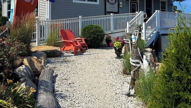 A two-story building with a balcony, a gravel driveway, and a red flag. - The Nest at Black Hall (Old Lyme)