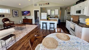 A spacious living area with a large wooden dining table, a kitchen with white cabinets and a microwave, and a ceiling fan. - The Nest at Black Hall (Old Lyme)
