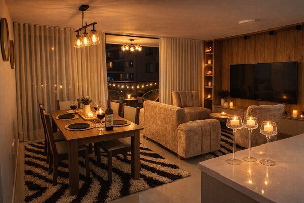 A modern living room with a dining area, a sofa, a TV, and candles on the table.