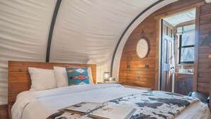 Une pièce aménagée avec une tente, un lit, une table de chevet, une lampe et une porte donnant sur l’extérieur.