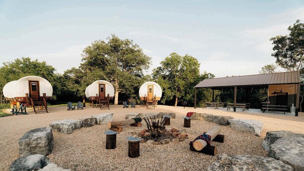 Un terrain de camping comprenant trois tentes en forme de dôme, un foyer et un espace de repos abrité.
