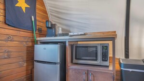 A compact kitchenette with a refrigerator, microwave, and wooden cabinets. - Cozy Couples Wagon | Lake Access + King bed (Branson)