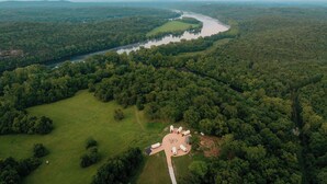 Vista aérea de una zona boscosa con un río, una explanada con estructuras dispuestas en círculo y un pequeño edificio.