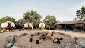 Un campamento con tres tiendas en forma de cúpula, un pozo de fuego y una zona de estar cubierta.