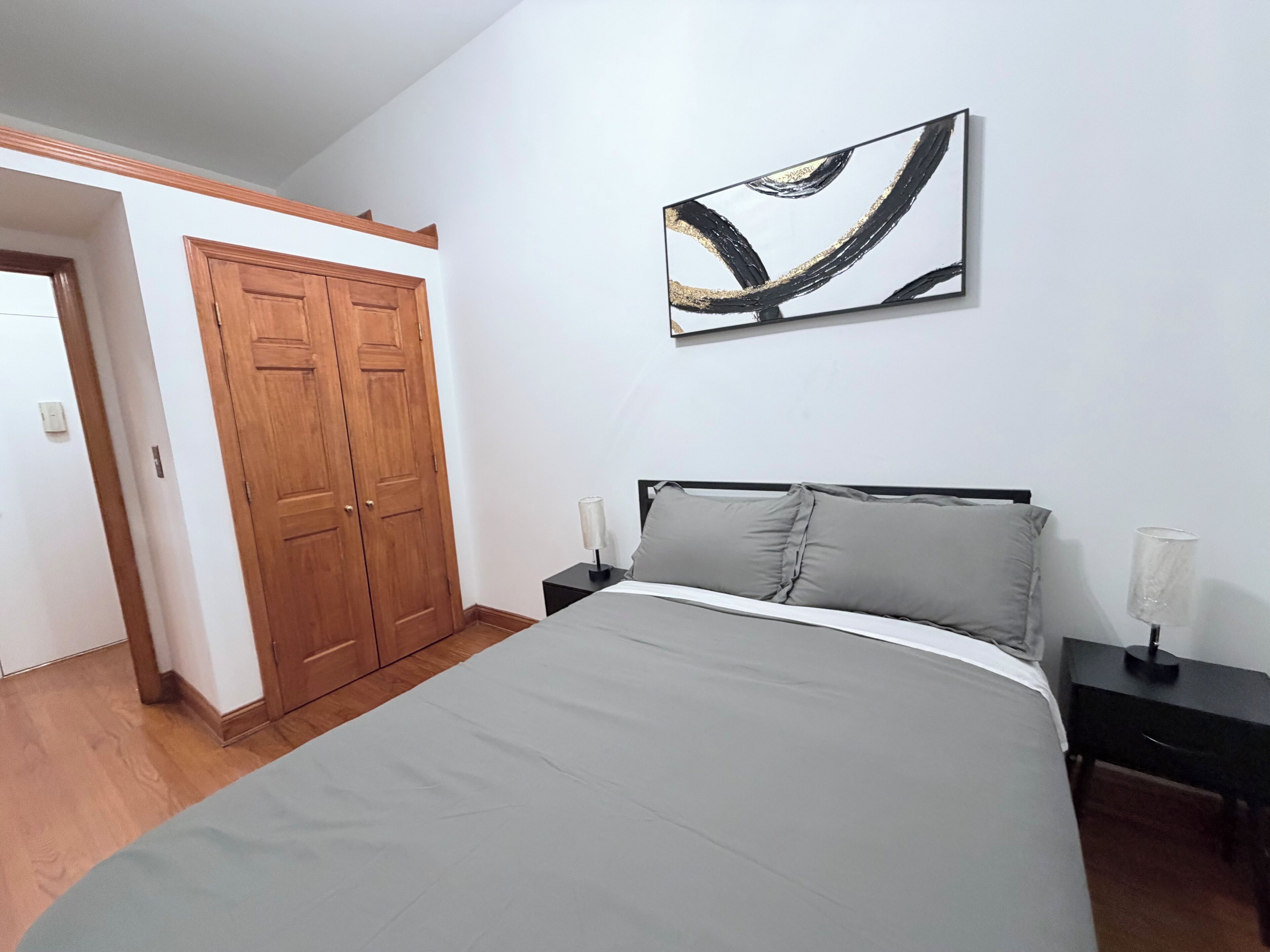 A bedroom with a bed, nightstands, a wall-mounted abstract art piece, and a wooden wardrobe.