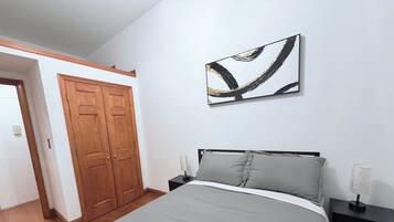 A bedroom with a bed, nightstands, a wall-mounted abstract art piece, and a wooden wardrobe.