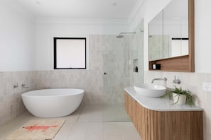 Een moderne badkamer met een vrijstaand bad, een wastafel met houten opbergmeubel en een grote spiegel.