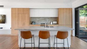 Eine moderne Küche mit Marmorarbeitsplatte, Holzschränken und drei Barhocker.