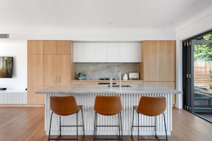 Eine moderne Küche mit Marmorarbeitsplatte, Holzschränken und drei Barhocker.